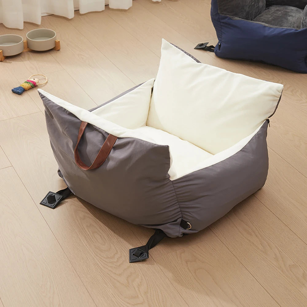 Grey and cream travel car seat bed with carry handles on a wooden floor
